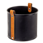 A cylindrical black container with vertical ridges and two brown leather handles, secured by silver rivets, is set against a white background. The Mini Planter with Leather Handle - Black - Medium by MyHomeDecor.ca has handles that extend slightly above its top, adding functionality and style to the sleek design.