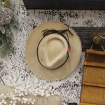 A Cowboy Hat Blond Small by MyHomeDecor.ca hangs on a wall adorned with monochromatic nature-themed wallpaper. Nearby, a wooden shelf and greenery decorations are visible, contributing to a rustic, cozy atmosphere that captures the essence of Western fashion.