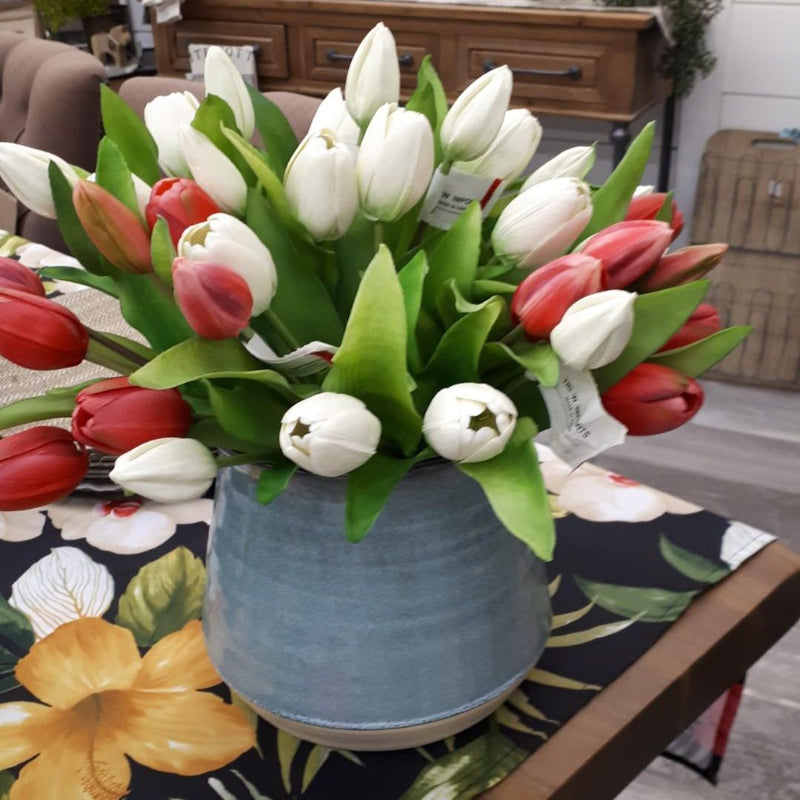 Fake tulip flowers in white and pink in a blue vase and green leafs