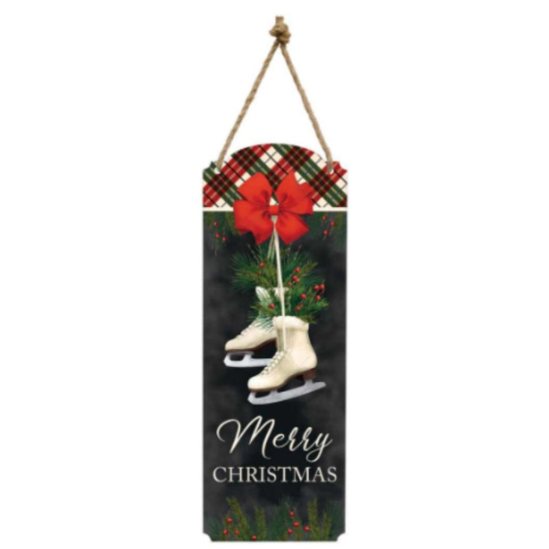 A piece of winter wall decor features a rustic rectangular sign with a plaid red and black ribbon at the top, a pair of hanging white ice skates, and a festive greenery arrangement. The text "Wall Plq Metal Merry Xmas" by MyHomeDecor.ca is written at the bottom in elegant script.